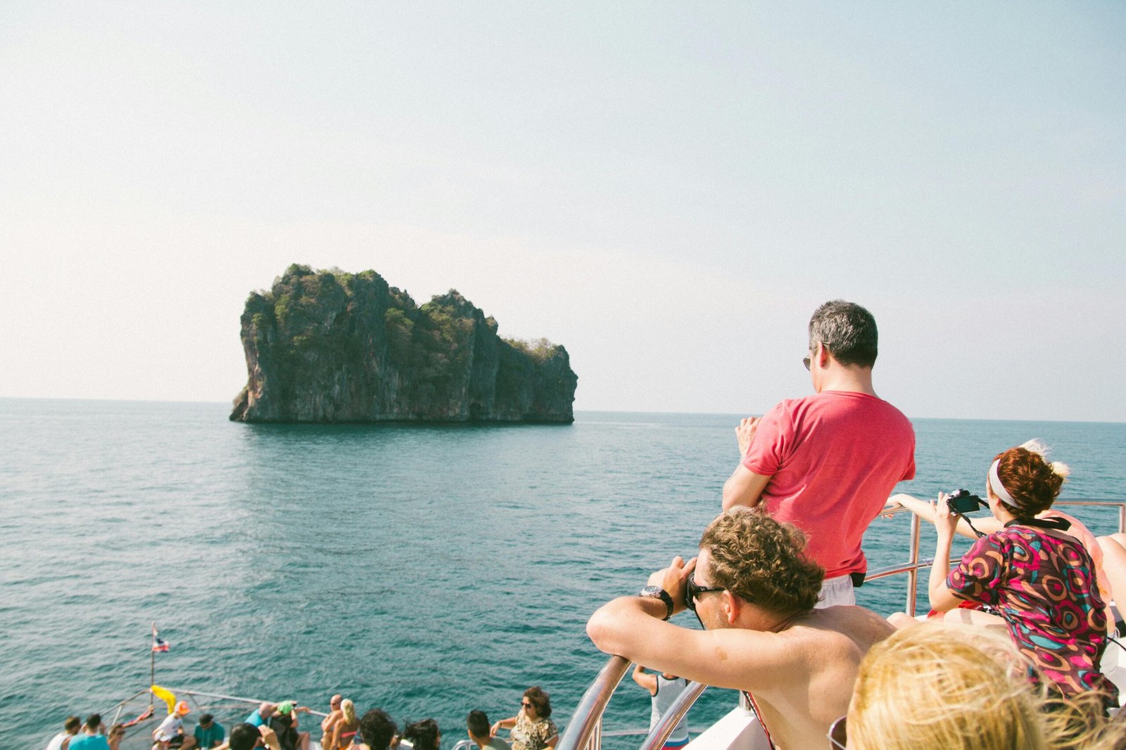 Tourists enjoying a scenic boat ride near a rocky island in the clear, blue ocean.